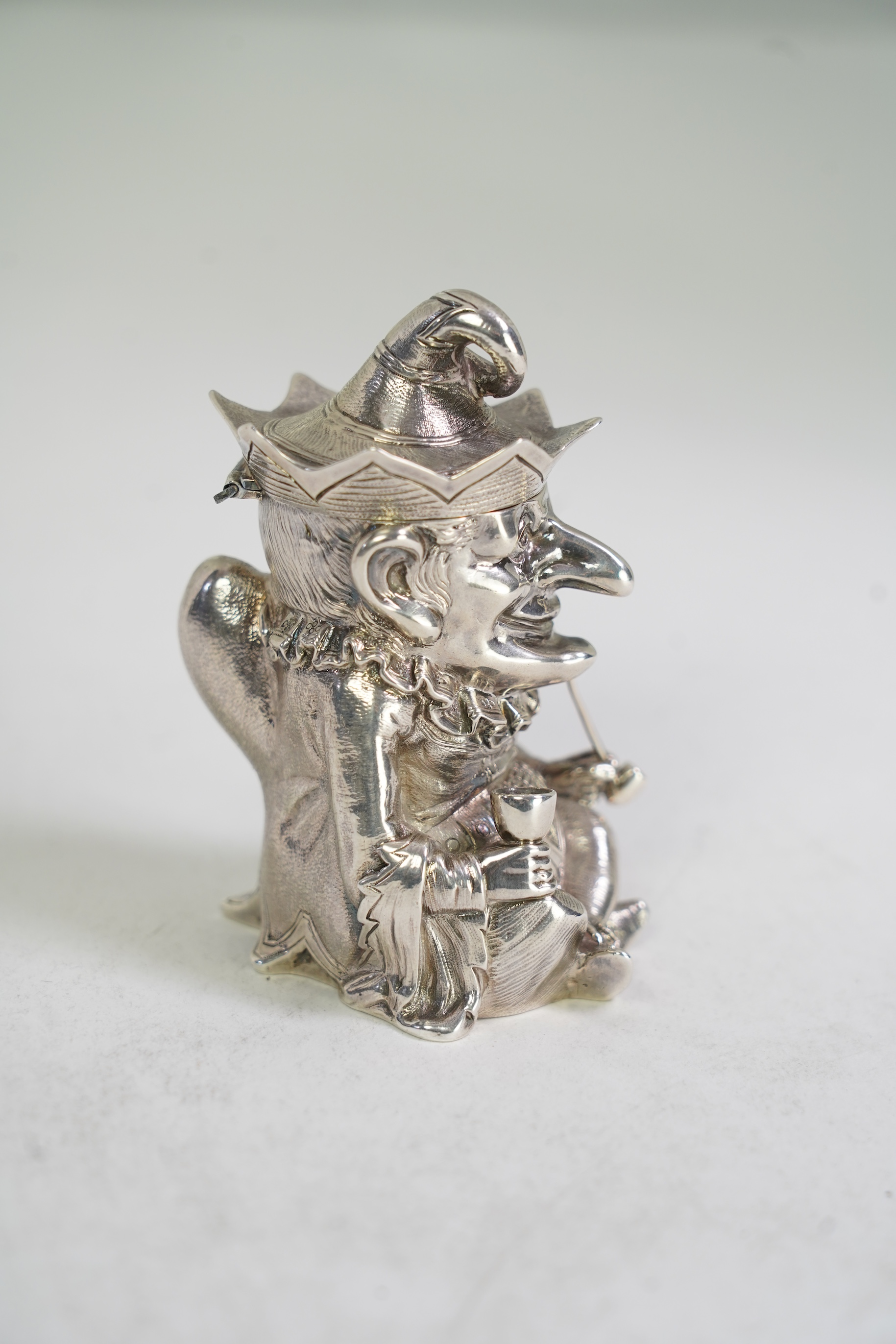 A rare Victorian novelty cast silver mustard pot, modelled as seated cross-legged Mr. Punch, holding a wine glass and smoking a pipe, by Robert Hennell III